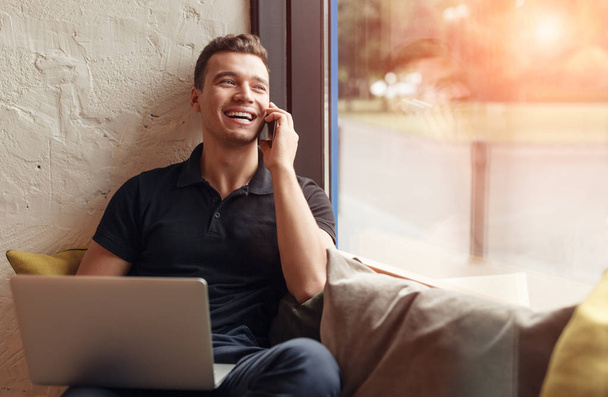 Laughing man with laptop speaking on phone - Foto, imagen