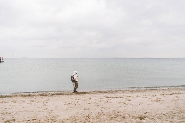 Yksi valkoihoinen mies nuori valkoihoinen nainen turisti musta reppu hiekkarannalla lähellä Itämerta talvella. Teemareissu yksin. Ajatuksia ja unelmia näköalalla horisonttiin
 - Valokuva, kuva