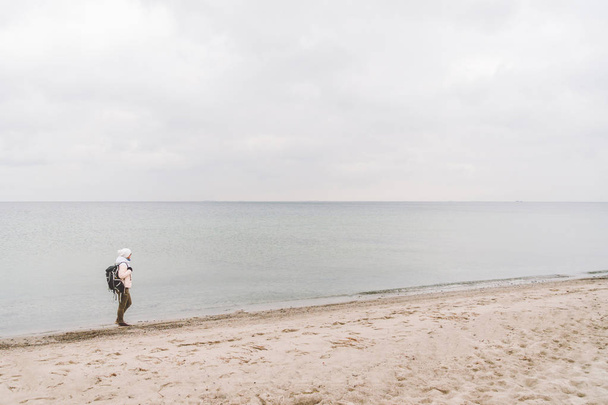Un hombre caucásico joven turista caucásico con una mochila negra en una playa de arena cerca del mar Báltico en invierno. Viaje temático solo. Pensamientos y sueños con vistas al horizonte
 - Foto, Imagen