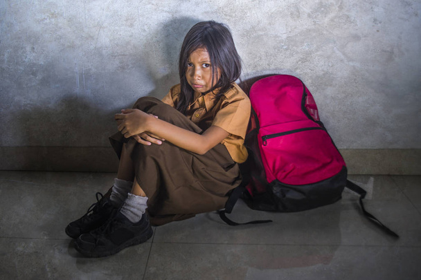 sad and depressed 8 or 9 years old child in school uniform sitting on the floor with her bad crying helpless feeling scared and desperate suffering bullying - Photo, Image