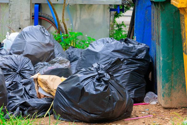 Stapel zwarte vuilnis langs de weg en regendruppels op de zak - Foto, afbeelding