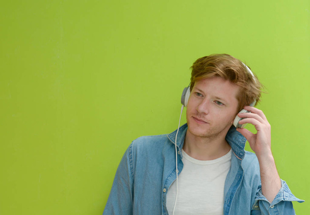 χαρούμενος νεαρός άνδρας να ακούτε μουσική με ακουστικά στην πράσινη β - Φωτογραφία, εικόνα