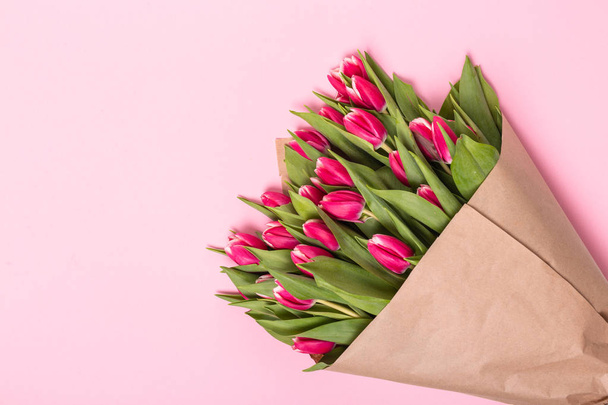 Różowe tulipany w papier pakowy na różowym tle. Widok płaski świeckich, top. - Zdjęcie, obraz