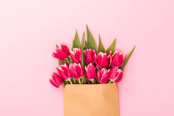 Blumengrüßkarte für die Frühlingsferien. zarte rosa Tulpen in einem Umschlag auf rosa Hintergrund - Foto, Bild