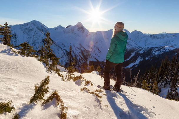 Caucasian adventurous girl snowshoeing on top of a mountain during a vibrant winter sunset. Taken on top of Zoa Peak near Hope, British Columbia, Canada. - Φωτογραφία, εικόνα