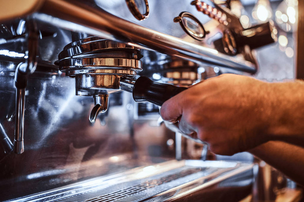 Foto de un barista sosteniendo un portafilter con un café negro molido y trabajando en una máquina de café en una cafetería o restaurante
 - Foto, Imagen