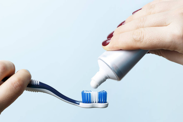 Жіноча рука тримає зубну щітку і стискає зубну пасту
 - Фото, зображення