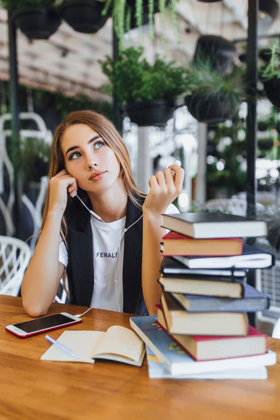young woman listening music on earphones near books at cafe - Photo, Image