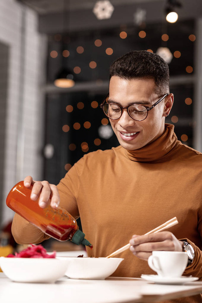 Young man adding ketchup to the food while holding the chopsticks with other hand. - Foto, imagen