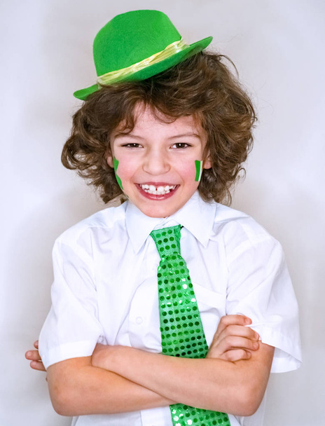 Hispanic child boy having fun during Saint Patrick celebrations over a light background. I am smiling a boy with a green shamrock and Irish flag on my cheek. Patrick's Day celebrations. - Valokuva, kuva