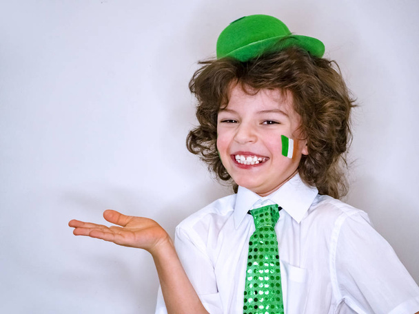 Saint Patrick celebrations over a light background. I am a smiling boy with a Irish flag on my cheek holding an imaginary subject in my hand. Copy space - Photo, Image