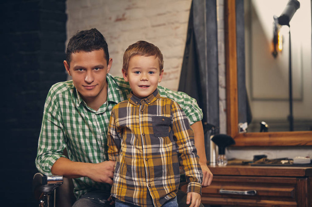 Young handsome father and his little stylish son at barbershop waiting for barber - Fotografie, Obrázek