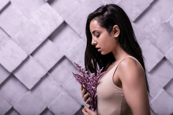 Profile studio photo of long-haired brunette girl cuddling lilac flowers - Fotó, kép