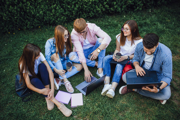 group of students doing homework, sitting on grass near campus - Фото, изображение