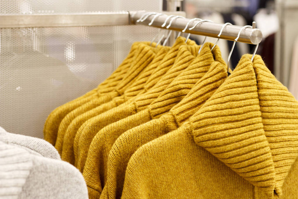 trendy Ceylon geel kleur wollen gebreide truien opknoping op hangers in de winkel, close-up - Foto, afbeelding