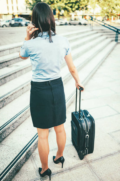 молодая деловая женщина, стоящая на улице с чемоданом
 - Фото, изображение