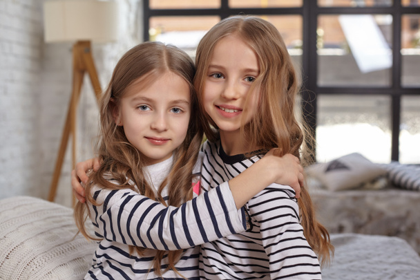 The image of two little sisters sitting on the bed in the room. - Foto, imagen