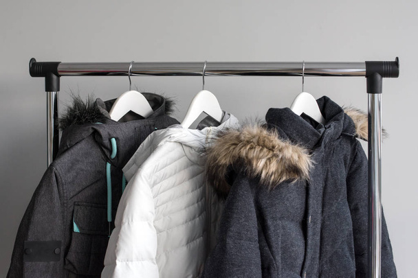 Hanger stand with warm jackets. Winter jackets with fur collar hang on white wooden hangers. Collection of winter jackets in shop. Winter season fashion background. - Photo, Image