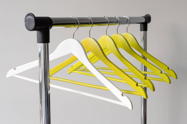 Empty clothes hangers on metal rail against grey background. Rectangular metal clothing rail with empty color wooden coat hangers. - Φωτογραφία, εικόνα