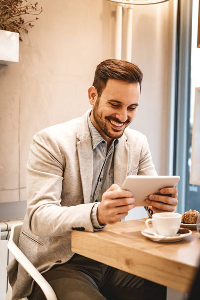 молодой улыбчивый человек, использующий цифровой планшет и пьющий кофе в кафе
 - Фото, изображение