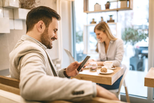 Homme utilisant smartphone et jeune femme souriante travaillant sur ordinateur portable et boire du café dans le café
 - Photo, image
