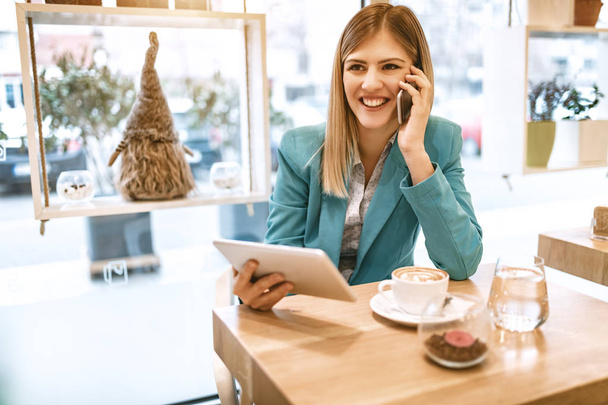 Jonge Glimlachende zakenvrouw op koffiepauze in café met behulp van tablet pc  - Foto, afbeelding