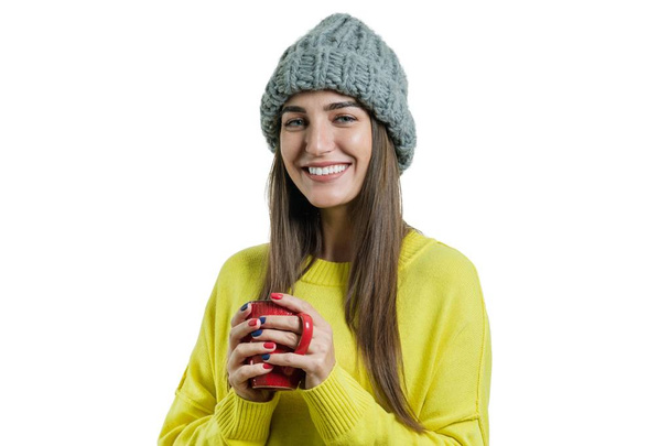 Portrait of smiling winter young woman in knitted hat, yellow sweater with cup of hot drink, isolated on white - Photo, image