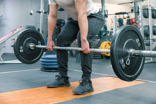 Closeup of arms and legs of man exercising with barbell at sport gym. Athlete, bodybuilding, training, weightlifting, workout exercises concept - Foto, Bild