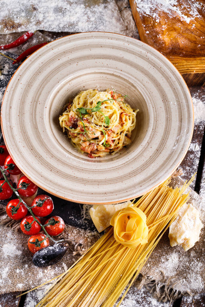 Pasta Carbonara with Parmesan cheese and sauce on a plate on a wooden background - Fotó, kép