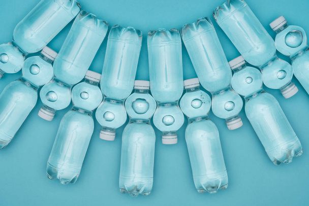 top view of transparent plastic water bottles arranged in rows isolated on turquoise - Fotoğraf, Görsel