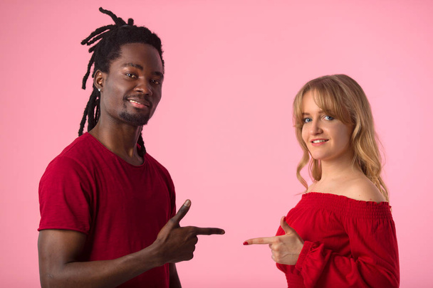 beautiful young couple african man and white woman in red t-shirts on pink background with hand gesture - Fotografie, Obrázek