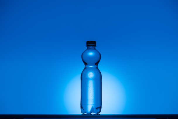 πιο ήπια εικόνα από πλαστικό μπουκάλι νερού σε neon μπλε φόντο με αντίγραφο χώρου και με οπίσθιο φωτισμό - Φωτογραφία, εικόνα