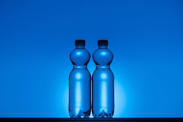 コピー スペースとバックライトの青いネオン背景に透明なプラスチックの水ボトルのトーンのイメージ - 写真・画像
