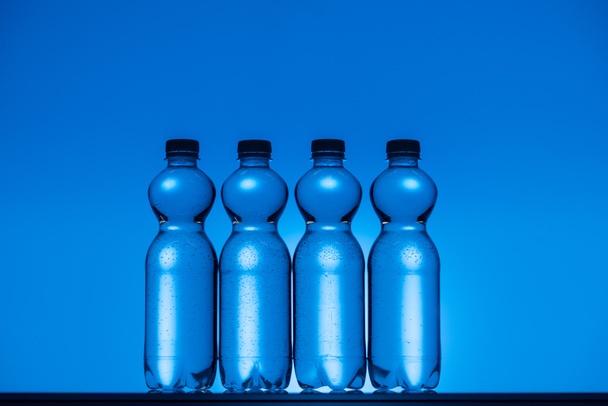 toned image of clear plastic water bottles on neon blue background with backlit - Foto, afbeelding