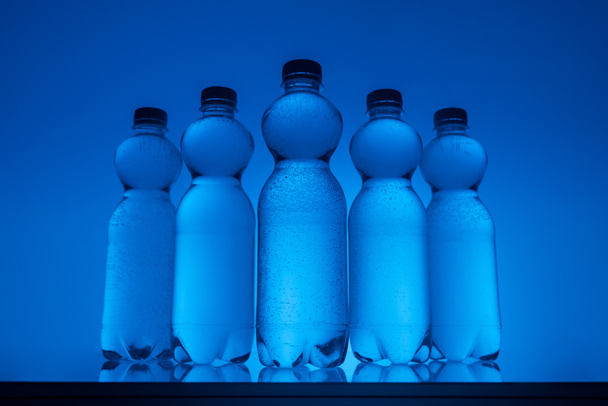 transparent water bottles in row on neon blue background - Photo, Image