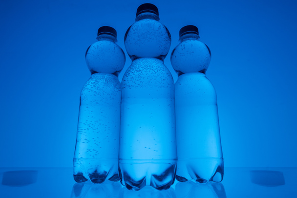 toned image of plastic water bottles in row on neon blue background - Foto, Imagem