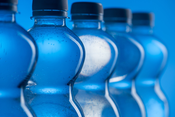close up of plastic water bottles with bubbles in row on blue background - Foto, afbeelding