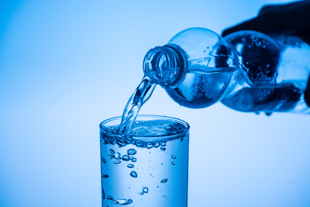 partial view of man pouring water from plastic bottle in glass on blue background - Foto, afbeelding