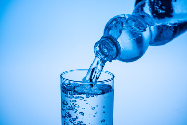 water pouring from plastic bottle in glass on blue background with copy space - Foto, Imagem