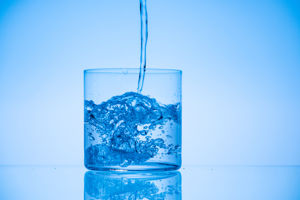 toned image of water pouring in drinking glass on blue backdrop with copy space - Photo, Image