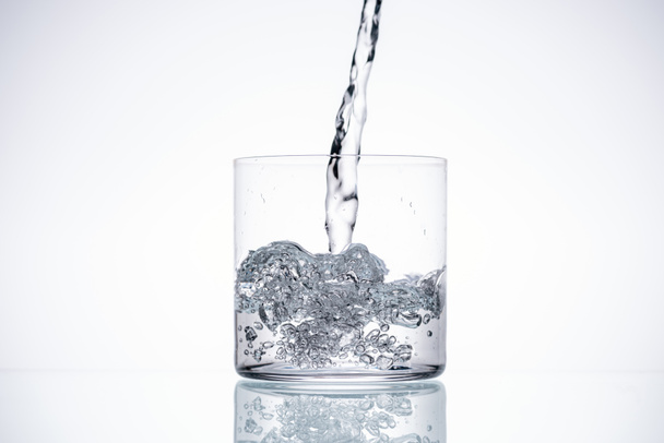 Wasser gießt in Glas auf weißem Hintergrund mit Hintergrundbeleuchtung und Kopierraum - Foto, Bild