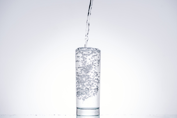 Wasser gießt in Glas auf weißem Hintergrund mit Hintergrundbeleuchtung - Foto, Bild