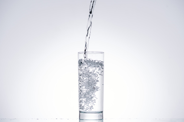 Hintergrund von Wasser gießt in Glas auf weiß mit Hintergrundbeleuchtung und Kopierraum - Foto, Bild