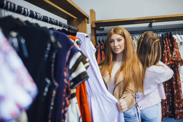Two young women shopping at modern fashion store, choosing clothes  - Photo, Image