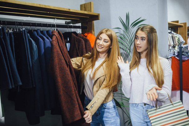 Twee jonge vrouwen winkelen bij moderne mode winkel, het kiezen van kleding  - Foto, afbeelding