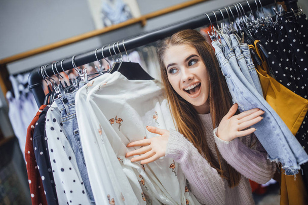Young beautiful woman getting pleasure from shopping and posing at rack with clothes - Valokuva, kuva