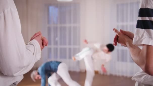 Taistelulajeja. Kaksi akrobaattinen mies suorittaa capoeira elementtejä, kun heidän oppilaansa taputus kädet
 - Materiaali, video