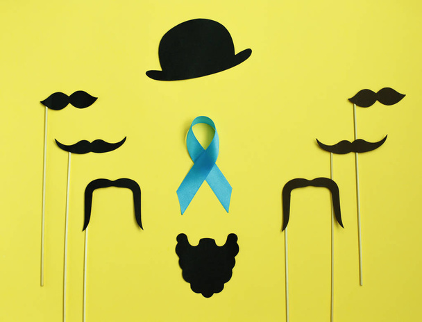 εικόνα ενός ανθρώπου στο χαρτί. Γένια και μουστάκι μπλε κορδέλα. σε κίτρινο φόντο. Έννοια του καρκίνου του προστάτη - Φωτογραφία, εικόνα