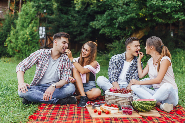 Happy friends having fun on picnic and eating fruits, focus on foreground - Фото, зображення