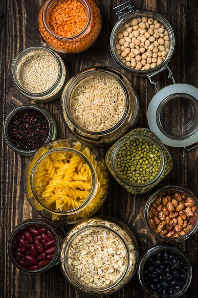 Obiloviny, luštěniny a fazole ve sklenicích na tmavý dřevěný stůl.  - Fotografie, Obrázek